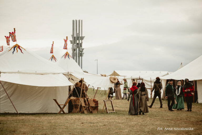 Białe namioty, rekonstruktorzy w historycznych strojach, sceny codziennego życia. W tle Pomnik Grunwaldzki.